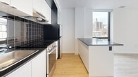 Located on Rue Sherbrooke Ouest in Montréal, this modern one-bedroom, one-bathroom unit offers a clean, contemporary design throughout. Light hardwood flooring runs continuously across the open-concept layout, complementing the crisp white walls and creating a bright, cohesive aesthetic.

The kitchen is efficiently designed with white flat-front cabinetry, dark countertops, a bold black tile backsplash, and stainless steel appliances including a range and refrigerator. A peninsula with a dark countertop extends into the living area, providing additional workspace and a natural division between the kitchen and living room. A track lighting fixture overhead adds a modern accent. Large windows flood the kitchen and living area with natural light while framing views of the surrounding Montréal cityscape.

The living room is open and airy, with floor-to-ceiling windows on two walls offering expansive city views and ample natural light. The bedroom is a well-proportioned private retreat featuring a large window with city views, light hardwood floors, and a sliding-door closet with built-in drawers for storage.

The bathroom is finished in crisp white square tile from floor to ceiling, featuring a modern floating vanity with an undermount sink, a mirrored medicine cabinet, and a walk-in shower, delivering a clean and functional design.