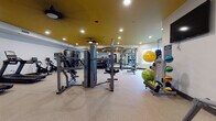 Located at 408 Northampton Rd in Amherst, Massachusetts, this fitness center is a fully outfitted, single-floor facility designed to support a wide variety of workout routines. The space features a distinctive design with bold gold-painted ceilings contrasting against clean white walls, recessed lighting, and ceiling fans that maintain a comfortable environment during workouts.

The cardio section is equipped with multiple treadmills and upright stationary bikes, all featuring digital display consoles. A row of elliptical cross-trainers and stair-climber machines rounds out the cardio offerings. Full-length mirrors line the walls throughout, enhancing the sense of openness and allowing users to monitor their form.

The strength training area is generously stocked with Matrix-brand cable machines, multi-functional cable crossover stations, and a comprehensive rack of dumbbells spanning a wide range of weights. Adjustable benches are positioned throughout for versatile use with free weights or machines. Functional training accessories, including stability balls, medicine balls, and resistance tools, are neatly organized on dedicated racks along the walls.

Natural light filters in through windows, complementing the recessed ceiling lights to create a bright, energizing atmosphere. The speckled rubberized flooring provides durability and safety underfoot. A wall-mounted flat-screen television adds an entertainment element to the space. Two entry doors provide easy access, making this fitness center a practical and inviting facility.
