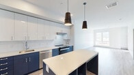 Located at 2695 S Water St in Pittsburgh's South Side neighborhood, this modern one-bedroom, one-bathroom unit offers a well-designed layout with contemporary finishes throughout. The open-concept kitchen and living area serves as the heart of the home, showcasing a striking two-tone kitchen with navy blue lower cabinets, crisp white upper cabinetry, and a white quartz countertop island with built-in open shelving. Stainless steel appliances, including a refrigerator, dishwasher, and range, complement the subway tile backsplash, while stylish pendant lighting adds a refined touch. Light wood-tone flooring flows seamlessly throughout the entire unit. The living area benefits from natural light through large windows. The bedroom is a well-proportioned retreat featuring large windows that frame elevated views of the Pittsburgh skyline and surrounding cityscape, along with a dedicated closet with sliding doors. The clean, bright bathroom includes a white vanity with quartz countertop, a large mirror, and a glass-enclosed walk-in shower, all finished with light wood-tone flooring that ties the space together cohesively.