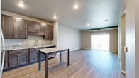 This thoughtfully designed one-bedroom, one-bathroom unit in Aberdeen, South Dakota offers a modern, move-in-ready layout with quality finishes throughout. The open-concept kitchen and living area serves as the heart of the space, where light hardwood-style flooring flows seamlessly underfoot. The kitchen is outfitted with rich dark-toned cabinetry, granite countertops, a central island with matching granite surface, and a full suite of stainless steel appliances including a refrigerator, range, microwave, and dishwasher — ideal for everyday cooking and entertaining. The living area is bright and airy, benefiting from a sliding glass door that opens to an outdoor balcony with neighborhood views, allowing natural light to fill the room. A hallway connects the main living space to the private bedroom, which features plush carpeting, a generous window overlooking the surrounding area, and exposed ductwork that adds an industrial accent. The bathroom is finished with granite countertops, dark wood cabinetry, a framed mirror, and includes accessibility grab bars. Neutral wall tones and consistent modern finishes create a cohesive, comfortable ambiance throughout this efficiently planned Aberdeen residence.