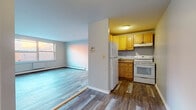 Located in Hartford, CT, this single-floor unit offers a practical and well-organized layout designed for comfortable everyday living. The open living area is finished with light-toned laminate wood flooring that runs throughout the main spaces, lending a clean and cohesive look. Natural light filters in through double-pane windows, and baseboard heating units line the walls, ensuring year-round comfort. The living space flows directly into a semi-open kitchen, which features warm honey-toned wood cabinetry, a white refrigerator, a white electric range, and a single-basin sink with a dark countertop — providing ample storage and functionality. A dedicated bedroom offers plush wall-to-wall carpeting, a window with natural light, and its own baseboard heating unit, creating a quiet and cozy retreat. The bathroom is neatly appointed with tile flooring, a white vanity with under-cabinet storage, a mirrored medicine cabinet, and a full bathtub with shower — all presented in a clean, neutral palette. Throughout the unit, the neutral gray and white walls contribute to a bright, airy atmosphere that is easy to personalize. The layout makes efficient use of space, with a clear sense of flow between the living, kitchen, and private areas of the home.