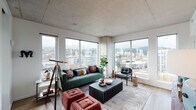 Located in the heart of Portland, Oregon, this contemporary high-rise residence at 1510 SW Alder St offers a sophisticated urban living experience defined by modern design and stunning city views. The open living area is anchored by expansive corner windows that stretch from floor to ceiling, flooding the space with natural light and framing breathtaking panoramic views of the Portland skyline and the surrounding West Hills. Exposed concrete ceilings lend an industrial character throughout, complemented by warm light wood flooring that runs seamlessly across the main living areas. The well-appointed kitchen features a sleek, two-tone design with dark lower cabinetry and crisp white upper cabinets, paired with stainless steel appliances including a gas range, built-in microwave, dishwasher, and a full-size refrigerator. Stone countertops and a white tile backsplash complete the polished, modern aesthetic. The bedrooms offer a tranquil retreat, each with large windows showcasing elevated city and hillside views, and plush carpeting underfoot. The bathrooms are thoughtfully designed with dark vanity cabinetry, stone countertops, wood-look tile flooring, and a mix of concrete and marble-style tile accents. This residence delivers a compelling blend of urban energy and refined interior comfort.