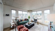 Located in the heart of Portland, Oregon, this contemporary high-rise residence at 1510 SW Alder St offers a sophisticated urban living experience defined by modern design and stunning city views. The open living area is anchored by expansive corner windows that stretch from floor to ceiling, flooding the space with natural light and framing breathtaking panoramic views of the Portland skyline and the surrounding West Hills. Exposed concrete ceilings lend an industrial character throughout, complemented by warm light wood flooring that runs seamlessly across the main living areas. The well-appointed kitchen features a sleek, two-tone design with dark lower cabinetry and crisp white upper cabinets, paired with stainless steel appliances including a gas range, built-in microwave, dishwasher, and a full-size refrigerator. Stone countertops and a white tile backsplash complete the polished, modern aesthetic. The bedrooms offer a tranquil retreat, each with large windows showcasing elevated city and hillside views, and plush carpeting underfoot. The bathrooms are thoughtfully designed with dark vanity cabinetry, stone countertops, wood-look tile flooring, and a mix of concrete and marble-style tile accents. This residence delivers a compelling blend of urban energy and refined interior comfort.