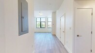 This well-appointed two-bedroom, one-bathroom residence in Boston's vibrant 02215 neighborhood offers a thoughtfully designed single-floor layout with a clean, contemporary aesthetic throughout. Light-toned hardwood flooring flows seamlessly across every room, complementing the crisp white walls and creating a bright, cohesive feel.

The open-plan living and kitchen area serves as the heart of the home. The kitchen features light wood cabinetry, white quartz countertops, stainless steel appliances including a refrigerator, range, and built-in microwave, and a peninsula that opens to the living space — ideal for both everyday living and entertaining.

The primary bedroom is generously proportioned, bathed in natural light from large black-framed windows that frame views of the surrounding neighborhood and tree canopy. The second bedroom also benefits from a black-framed window, maintaining the same bright and airy character. A dedicated closet provides convenient storage.

The bathroom is finished with modern tile work and features a frameless sliding glass walk-in shower with mosaic tile flooring, offering a clean and refined aesthetic. A hallway connects the living areas to the private spaces, keeping the layout functional and organized. The overall ambiance is modern, minimal, and light-filled throughout.