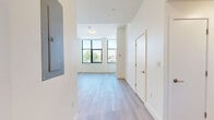 This well-appointed two-bedroom, one-bathroom residence in Boston's vibrant 02215 neighborhood offers a thoughtfully designed single-floor layout with a clean, contemporary aesthetic throughout. Light-toned hardwood flooring flows seamlessly across every room, complementing the crisp white walls and creating a bright, cohesive feel.

The open-plan living and kitchen area serves as the heart of the home. The kitchen features light wood cabinetry, white quartz countertops, stainless steel appliances including a refrigerator, range, and built-in microwave, and a peninsula that opens to the living space — ideal for both everyday living and entertaining.

The primary bedroom is generously proportioned, bathed in natural light from large black-framed windows that frame views of the surrounding neighborhood and tree canopy. The second bedroom also benefits from a black-framed window, maintaining the same bright and airy character. A dedicated closet provides convenient storage.

The bathroom is finished with modern tile work and features a frameless sliding glass walk-in shower with mosaic tile flooring, offering a clean and refined aesthetic. A hallway connects the living areas to the private spaces, keeping the layout functional and organized. The overall ambiance is modern, minimal, and light-filled throughout.