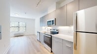 This thoughtfully designed studio unit at 10 W Westfield Ave in Roselle Park, NJ, offers a clean, modern aesthetic with efficient use of space. The open-concept layout seamlessly connects the kitchen and dining area, creating a bright and functional living environment. Light wood-style flooring runs throughout the main living areas, complementing the crisp white walls and contributing to an airy, contemporary feel.

The kitchen is a standout feature, outfitted with sleek flat-front cabinetry in a warm gray tone, white quartz countertops, and a geometric hexagonal tile backsplash. Stainless steel appliances — including a range, over-the-range microwave, dishwasher, and refrigerator — provide a polished, modern finish. Track lighting above the kitchen adds both style and functionality.

The bathroom continues the modern design language with light tile flooring, a gray vanity with a white countertop, a glass-enclosed shower, and accessibility grab bars along the walls. A dedicated closet and utility room add practical storage and convenience to the unit.

Natural light filters through the window in the living area, brightening the open space. The white-painted walls and minimalist design create a neutral, versatile canvas throughout this well-appointed studio.
