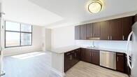 This thoughtfully laid-out one-bedroom, one-bathroom unit offers a cohesive and modern living experience across a single floor. The open-concept kitchen and living area serves as the heart of the space, featuring rich dark-espresso cabinetry with sleek stainless steel hardware, granite countertops, a classic white subway tile backsplash, and a full suite of stainless steel appliances including a dishwasher, range, microwave, and refrigerator. A peninsula provides additional counter space and creates a natural division between the kitchen and the living area. Light hardwood-style flooring runs throughout, lending warmth and visual continuity. The living area is bright and open, benefiting from large windows that invite natural light. The bedroom is a comfortable retreat, highlighted by a window framing city views and a double-door closet offering ample storage. The bathroom is finished with tile flooring, a granite-topped dark vanity, a large mirror, and a full soaking tub with tiled surround. A hallway connects the rooms efficiently, completing the clean, functional layout. Neutral wall tones throughout create a calm, versatile backdrop suited to a variety of furnishing styles.