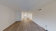 This well-appointed 2-bedroom residence is laid out on a single floor, offering a practical and comfortable living environment. The interior is unified by light wood-tone laminate flooring that runs throughout the main living areas and bedrooms, complemented by crisp white walls that give each room a clean, modern feel.

The living room is a generously proportioned open space with a front entry door and easy access to the rest of the unit. A large sliding glass door at the far end fills the room with natural light and provides views of an outdoor balcony area. The space flows naturally into the hallways that connect to the bedrooms and kitchen.

The primary bedroom is notably spacious, featuring a ceiling fan with light fixture, a large window with vertical blinds that frame a lush outdoor view, and ample room for furnishings. The secondary bedroom is a comfortable, well-lit space with its own window dressed in vertical blinds.

The kitchen is efficiently designed with white shaker-style cabinetry, granite-look countertops, tile flooring, stainless steel appliances including a dishwasher and built-in microwave, and a double sink positioned beneath a window with a pleasant outdoor view. The layout maximizes counter and storage space throughout.

Overall, the unit presents a bright, neutral aesthetic with consistent finishes and functional design across every room.