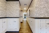 Located at 698 Basilica Bay Drive in Spring, TX, this dedicated mailroom hallway is a compact yet thoughtfully designed shared amenity space. The room is defined by its striking black-and-white geometric patterned wallpaper, which covers the upper portion of the walls and creates a bold visual focal point throughout the space. A dark horizontal trim band divides the decorative wallpaper from the lower wall sections, adding a clean, structured contrast to the overall design.

Built-in white mailbox units line the walls in an L-shaped configuration, offering a generous number of individual compartments that are neatly organized and uniformly finished. The crisp white cabinetry of the mailboxes complements the monochromatic wallpaper for a cohesive aesthetic. Wood-look tile flooring runs throughout, providing a warm, durable surface that anchors the space with a residential feel.

Framed artwork is displayed along the upper walls, adding a decorative touch that elevates the space beyond purely functional use. A glass-paneled entry door allows natural light to filter in, brightening the interior. Recessed ceiling lighting ensures consistent illumination throughout. A floating shelf with decorative greenery and accents adds a welcoming, homey detail. The overall ambiance is polished and modern, balancing practicality with intentional design.