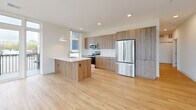 Located at 8530 W National Ave in West Allis, WI, this thoughtfully designed single-floor unit offers three bedrooms, three bathrooms, and a seamless modern aesthetic throughout. Light-toned hardwood flooring flows through the main living areas, complemented by crisp white walls and recessed lighting that create a clean, airy atmosphere.

The living area is a standout, featuring expansive floor-to-ceiling windows that flood the space with natural light and frame views of the surrounding greenery and streetscape. The kitchen is well-equipped with rich wood cabinetry, white quartz countertops, stainless steel appliances including a range and over-the-range microwave, a white subway tile backsplash, and a window that brings in additional natural light.

The three bedrooms are carpeted for comfort, each offering generous proportions and easy access to the hallway. The primary bedroom includes a dedicated closet, while all bedrooms benefit from proximity to the three full bathrooms. The bathrooms are finished with wood-toned vanities, white countertops, and light wood-style flooring. One bathroom features a glass-enclosed walk-in shower, while another offers a full soaking tub with shower combination.

Hallways are bright and efficiently laid out, with sliding closet doors and recessed lighting tying together the home's cohesive contemporary design.
