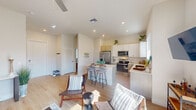 This well-designed single-floor residence offers a cohesive, contemporary aesthetic throughout, characterized by light-toned walls, smooth ceilings with recessed lighting and ceiling fans, and warm light wood flooring that runs seamlessly through every room.

The open-concept living and kitchen area forms the heart of the home. The kitchen is outfitted with stainless steel appliances — including a side-by-side refrigerator, electric range, and over-the-range microwave — complemented by white upper cabinetry, warm wood-toned lower cabinets, and light quartz countertops. A central island with bar seating provides a casual dining option. The living area flows naturally from the kitchen and features a sliding glass door that opens to a private outdoor patio, bringing in generous natural light and extending the sense of space.

The primary bedroom is generously proportioned with vaulted ceilings, a bright window, and direct access to a well-appointed en-suite bathroom. The en-suite includes a dual-sink vanity with quartz countertops, wood-toned cabinetry, a large wall mirror, and a glass-enclosed walk-in shower. A second bedroom is equally comfortable, featuring large windows and a ceiling fan. A second full bathroom with a tub-shower combination and wood-toned vanity serves this room. Throughout, the design is clean, modern, and efficiently laid out.