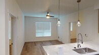 This well-designed single-floor unit offers a clean, contemporary aesthetic throughout its thoughtfully laid-out spaces. The open-concept kitchen and living area serves as the heart of the home, where a peninsula with a white quartz countertop and an undermount sink anchors the space. Stainless steel appliances — including a refrigerator, electric range, microwave, and dishwasher — are complemented by a two-tone cabinetry scheme featuring warm wood upper cabinets and cool gray lower units, along with a classic subway tile backsplash. Stylish pendant lights hang above the peninsula, adding a modern touch. The adjacent living area benefits from natural light through blinds-fitted windows and is equipped with a ceiling fan. Warm-toned hardwood-style flooring flows seamlessly throughout the entire unit, creating a cohesive and inviting atmosphere. The bedroom is a bright, comfortable space with its own ceiling fan and window with blinds. The bathroom is finished with a white quartz vanity, a large mirror, and a walk-in shower, maintaining the unit's consistent modern and minimalist design language. Overall, this unit presents a fresh, functional, and stylish living environment.