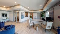 This single-floor amenity center is thoughtfully designed to offer residents a comprehensive range of facilities within a cohesive, contemporary aesthetic. The welcoming reception area greets visitors with light hardwood flooring, tray ceilings with decorative crown molding, recessed lighting, and an elegant multi-tiered chandelier. A staffed front desk is flanked by navy blue accent chairs and coastal-inspired artwork, setting a polished yet relaxed tone throughout.

Adjacent to the lobby, a business center provides two dedicated computer workstations along a built-in desk, accented by abstract artwork and natural light from large windows. A pool table is visible nearby, transitioning into a dedicated game room featuring poker tables positioned before expansive windows overlooking the outdoor courtyard.

The lounge area offers generous seating arrangements beneath stylish drum pendant lighting, complemented by a bar-height counter and tufted banquette seating. A private meeting room features a glass-top round table, upholstered armchairs, bold large-scale artwork, and a wall-mounted television.

A salon with bold geometric wallcovering provides styling chairs and media entertainment. The spacious fitness center is equipped with cardio machines, strength equipment, mirrored walls, ceiling fans, and large windows that flood the space with natural light.