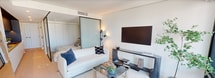 First Light #2401 is a thoughtfully designed 450-square-foot, one-bedroom, one-bathroom residence that maximizes every inch of its single-floor layout with sleek, contemporary finishes. The open living area is anchored by floor-to-ceiling windows that flood the space with natural light and frame sweeping city and waterfront views. Light hardwood flooring runs throughout, complementing a clean, neutral palette accented by dark bronze hardware and trim details. A glass partition with a sliding panel system elegantly divides the living area from the 330-square-foot bedroom, maintaining an open, airy feel while offering privacy. The kitchen features warm wood cabinetry and integrated appliances along a compact, functional corridor. The bathroom is a standout, showcasing full terrazzo wall and floor cladding, a glass-enclosed walk-in shower with both a rain head and handheld fixture, and a built-in soaking tub — all finished with brushed dark bronze fixtures. The private balcony, accessible from the living area, offers a serene outdoor retreat elevated among the city skyline, complete with glass railings that preserve unobstructed panoramic views. This unit combines refined urban design with efficient, intelligent use of space.