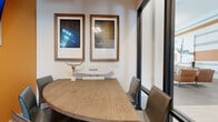 This sophisticated single-floor commercial space blends modern design with thoughtful functionality, creating an environment that is both professional and visually engaging. The open layout connects distinct zones seamlessly, with light wood-toned flooring flowing throughout the main areas and anchoring the overall aesthetic.

The main lounge area features a neutral, contemporary palette with plush seating, layered textiles, and carefully selected wall art, while decorative mirrors add depth and dimension to the space. A striking orange accent wall introduces a bold pop of color and serves as a visual focal point, complemented by a mounted display screen ideal for communications or presentations.

A dedicated meeting room offers an intimate yet polished setting, centered around a curved natural wood table surrounded by sleek upholstered chairs. Framed artwork with intricate patterned details adorns the walls, while floor-to-ceiling glass partitions maintain an open, connected feel without sacrificing privacy.

A cozy banquette nook is finished with plush mauve seating and marble-topped accent tables, illuminated by warm Edison-style wall sconces and a multi-globe pendant light, creating an inviting retreat within the broader space. Throughout, black-framed glass doors and partitions lend a refined, contemporary edge, tying together the various zones with consistent architectural detail and a polished, cohesive design sensibility.
