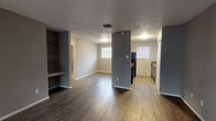 This single-story, 2-bedroom, 1-bathroom home offers a practical and well-organized layout designed for comfortable everyday living. The open-concept living and dining area is finished with dark hardwood-style flooring that extends throughout the main living spaces, complemented by neutral gray walls and a textured ceiling. A built-in shelving unit adds a distinctive architectural touch to the living area, providing convenient storage and display space. A structural column visually separates the living area from the kitchen zone while maintaining an open feel. Natural light filters in through multiple windows fitted with blinds, brightening the space throughout the day.

The kitchen is equipped with dark cabinetry, laminate countertops, and black appliances including a refrigerator and range, along with a window that allows additional natural light. The layout flows efficiently for everyday meal preparation.

Both bedrooms are finished with plush carpeting and feature ceiling fans with integrated lighting, creating a comfortable and functional retreat. Each room offers ample wall space and benefits from natural light through well-placed windows.

The bathroom includes a full tub and shower combination with classic white tile surround. Throughout the home, consistent gray tones and clean finishes create a cohesive, move-in-ready atmosphere.