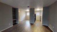 This single-story, 2-bedroom, 1-bathroom home offers a practical and well-organized layout designed for comfortable everyday living. The open-concept living and dining area is finished with dark hardwood-style flooring that extends throughout the main living spaces, complemented by neutral gray walls and a textured ceiling. A built-in shelving unit adds a distinctive architectural touch to the living area, providing convenient storage and display space. A structural column visually separates the living area from the kitchen zone while maintaining an open feel. Natural light filters in through multiple windows fitted with blinds, brightening the space throughout the day.

The kitchen is equipped with dark cabinetry, laminate countertops, and black appliances including a refrigerator and range, along with a window that allows additional natural light. The layout flows efficiently for everyday meal preparation.

Both bedrooms are finished with plush carpeting and feature ceiling fans with integrated lighting, creating a comfortable and functional retreat. Each room offers ample wall space and benefits from natural light through well-placed windows.

The bathroom includes a full tub and shower combination with classic white tile surround. Throughout the home, consistent gray tones and clean finishes create a cohesive, move-in-ready atmosphere.