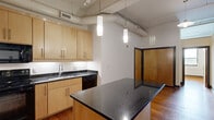 Located at 132 North Sycamore Street in Petersburg, VA, this two-bedroom, two-bathroom loft-style unit showcases a compelling blend of industrial and modern design. Soaring ceilings with exposed ductwork, pipes, and track lighting define the open living and kitchen area, lending the space a distinctive urban character. Rich hardwood floors flow throughout the main living areas and bedrooms, adding warmth that balances the industrial aesthetic.

The kitchen is well-appointed with light maple cabinetry, dark granite countertops, and black appliances, including a refrigerator, electric range, microwave, and dishwasher. A central island with pendant lighting above serves as both a prep space and a natural gathering point. Structural steel columns in the open living area further accentuate the loft-inspired design.

Both bedrooms feature the same warm hardwood flooring and tall ceilings, with the primary bedroom offering double closets. The bedrooms benefit from clerestory-style glazing above the interior walls, allowing light to filter through the space. Each of the two bathrooms is finished with tile flooring, maple vanities, granite countertops, and a tub-shower combination. A dedicated closet provides additional storage. The overall ambiance is modern and functional, with industrial touches that give the space a unique, loft-like character.
