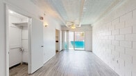 Located at 207 NW 17th St in Gainesville, Florida, this single-floor unit offers a practical and straightforward layout. The main living area is defined by white-painted concrete block walls, wood-look vinyl flooring, and a textured ceiling with an overhead ceiling fan. A sliding glass door floods the space with natural light and provides direct access to an outdoor balcony, offering views of the surrounding area. A wall-mounted air conditioning unit ensures climate control throughout.

The kitchen is efficiently designed, featuring white cabinetry, dark laminate countertops, a stainless steel sink, and a coil-burner electric range. A full-size refrigerator is housed in an adjacent area near the unit's entrance. Exposed beam ceilings add a subtle architectural detail to the secondary rooms.

The bathroom is clean and functional, outfitted with a tiled shower-tub combination, a wall-mounted sink, a toilet, and a mirrored medicine cabinet with overhead lighting. Wood-look flooring continues throughout, providing a cohesive aesthetic.

Overall, the unit presents a bright, no-frills interior with a neutral white palette, making it a practical living space well-suited for those seeking a straightforward, functional home in Gainesville.