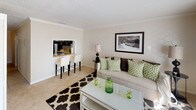 This two-floor residence offers a thoughtfully designed layout that balances functionality and comfort throughout its various living spaces. The kitchen features a U-shaped configuration with dark espresso cabinetry, light countertops, tile flooring, and black appliances including a range and built-in microwave. A pass-through window connects the kitchen to the living area, where a breakfast bar with seating provides a casual dining option.

The living room is finished with plush carpet, crown molding, and a textured ceiling, creating a warm and inviting atmosphere. Adjacent to the living area, the dining space accommodates a round glass-top table beneath a pendant light fixture, with wainscoting detail adding architectural interest to the walls.

Multiple bedrooms are present throughout the home. One features gray accent walls, carpet, and a window dressed with layered curtains, while another offers warm neutral tones, a ceiling fan with light fixture, and a spacious closet. The bathroom includes tile flooring, a tub-shower combination with decorative tile accents, and dark vanity cabinetry. A dedicated laundry area houses a full-sized washer and dryer with overhead shelving for added storage convenience.
