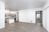 This single-floor residence offers a thoughtfully designed layout with contemporary finishes throughout. The open-concept entry leads directly into the living area, which features rich, dark hardwood-style flooring, crisp white walls, and a sliding glass door fitted with vertical blinds that allows natural light to pour in while providing outdoor views. A separate window further enhances the brightness of the living space.

The kitchen is a standout feature, showcasing light wood-grain cabinetry, neutral quartz-style countertops, a glossy tile backsplash, and a full suite of stainless steel appliances including a range, dishwasher, and microwave. A central island provides additional prep and seating space, making the kitchen both functional and inviting.

The bedrooms are carpeted for comfort and equipped with ceiling fans. Large windows fitted with horizontal blinds offer ample natural light and pleasant outdoor views, creating a calm and airy atmosphere.

Two bathrooms serve the unit. One includes a combination tub and shower with clean white tile surround, while the second features a walk-in shower with frosted glass doors. Both bathrooms are finished with modern vanities, grey countertops, wood-toned cabinetry, and sleek wall-mounted lighting. The space presents a clean, modern aesthetic throughout.