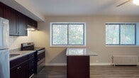 This single-floor unit offers a thoughtfully designed layout that balances comfort and functionality. The open-concept living and dining area features durable wood-look vinyl plank flooring, crown molding, and a ceiling fan with integrated lighting. Large windows fitted with blinds frame lush tree views, filling the space with natural light. A classic cast-iron radiator provides efficient heating.

The kitchen is well-equipped with rich dark espresso cabinetry, granite countertops, a white subway tile backsplash, a stainless steel refrigerator, and a stainless steel range. A central kitchen island with a granite top extends the counter space and provides a casual dining option, seamlessly connecting the kitchen to the living area.

The bedroom is a comfortable, carpeted retreat with neutral-toned walls, a window overlooking greenery, and a cast-iron radiator, creating a cozy atmosphere.

The bathroom is clean and bright, featuring an all-white tub and shower combination, a white vanity, and a window that introduces natural light into the space.

Overall, the unit presents a cohesive, updated aesthetic with practical finishes and a warm, inviting ambiance throughout.