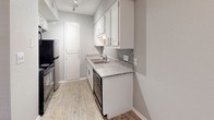 Located at 801 Capitol Ct in Austin's 78756 zip code, this single-story unit presents a cohesive, neutral aesthetic throughout its rooms. The layout, visible in the floor plan scan, reveals a thoughtfully arranged interior with distinct living, sleeping, kitchen, and bathroom areas.

The entry area features light wood-look flooring, crown molding, a ceiling fan with lighting, and a built-in window seat that brings in natural light through slatted blinds. This welcoming space connects to the rest of the unit with clean sightlines and consistent gray-toned walls throughout.

A secondary room also showcases the same wood-look flooring, crown molding, and a ceiling fan, offering a versatile space adaptable for various uses. An additional carpeted room provides a softer underfoot feel, also equipped with a ceiling fan and neutral walls.

The galley-style kitchen is well-appointed with white cabinetry, granite-look countertops, a gray subway tile backsplash, stainless steel appliances, a double sink, and light wood-look tile flooring. Track lighting overhead enhances functionality in this efficient cooking space.

The bathroom features granite-topped vanity cabinetry, a framed mirror, textured walls, and a full tub and shower combination with white tile surround, completing the unit's practical and consistent design.