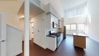 This thoughtfully designed two-story residence offers two bedrooms and two bathrooms across a well-appointed floor plan. The main level features an open living and kitchen area with soaring double-height ceilings that flood the space with natural light through large upper windows. The contemporary kitchen is outfitted with stainless steel appliances, including a gas range, built-in microwave, and dishwasher, complemented by sleek white cabinetry, dark countertops, and a geometric hexagonal tile backsplash. Rich hardwood flooring runs throughout the main level, adding warmth to the modern aesthetic. A staircase connects the two floors, leading to the upper level where the bedrooms are located. Both bedrooms feature plush carpeting and generous natural light from large windows. One bedroom opens directly onto a private outdoor terrace with wood-tile decking and expansive city views. A spacious walk-through area on the upper level provides built-in shelving and closet space. The two bathrooms are finished with neutral tile, including one featuring a glass-enclosed corner shower and the other offering a clean, minimalist design with vanity storage. The overall ambiance is clean, bright, and contemporary throughout.