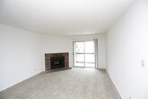 This single-floor residence offers a practical and comfortable layout across several distinct living areas. The spacious living room serves as the heart of the home, anchored by a classic brick fireplace and a sliding glass door that opens to a balcony, allowing natural light to fill the room. Neutral-toned carpet flows throughout the living and bedroom areas, contributing to a warm, cohesive feel.

The kitchen features light wood-toned laminate countertops that wrap around a corner layout, providing generous workspace. Dark wood cabinetry offers ample storage both above and below the counter, and a stainless steel sink with a built-in dishwasher adds everyday convenience. A pass-through window connects the kitchen to the adjacent living area.

The bedrooms are well-proportioned, with one room featuring two side-by-side bifold closets, and another offering a walk-in closet with built-in shelving. The primary bathroom includes an extended dark wood vanity with a white countertop, a large mirror, and tile-style flooring, while a second bathroom mirrors a similar vanity design with access to additional closet space. Throughout, the space maintains a clean, neutral palette.