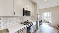 Located at 1457 N Main St in Los Angeles, CA, this thoughtfully designed one-bedroom, one-bathroom unit maximizes every inch of its compact footprint with a clean, modern aesthetic. Light hardwood flooring runs throughout, creating a cohesive and bright atmosphere across all rooms.

The open kitchen and living area serves as the heart of the unit. The kitchen features white upper cabinetry and soft grey lower cabinets, all accented with matte black hardware. A classic white subway tile backsplash frames the cooking area, while quartz countertops provide a crisp, clean workspace. Stainless steel appliances — including a range, over-the-range microwave, dishwasher, and refrigerator — complete the fully equipped kitchen. A small dining area with a round table sits adjacent, bathed in natural light from a nearby window.

The bedroom offers a cozy and restful retreat, accessed via a stylish sliding barn door that adds a contemporary architectural touch. Built-in open shelving flanks the entrance, providing practical storage. Natural light filters in, illuminating the space warmly.

The bathroom maintains the unit's modern palette with all-white finishes, a backlit vanity mirror, a soaking tub with shower, and matte black fixtures and accessories. The overall ambiance of the unit is clean, minimal, and functional — ideal for urban living in the heart of Los Angeles.