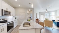 This single-story residence is thoughtfully designed with a modern aesthetic, combining functionality and style throughout its open layout. The kitchen serves as a central hub, showcasing white shaker cabinetry extending to the ceiling, granite countertops, and a full suite of stainless steel appliances, including a French door refrigerator, electric range, and built-in microwave. A large center island with an undermount sink, pendant lighting above, and bar seating makes it ideal for both meal preparation and casual dining. Light wood-tone flooring flows seamlessly from the kitchen into the open living area, which is bathed in natural light from large windows and a glass-panel exterior door. A ceiling fan overhead adds both form and function to this welcoming space.

The two bedrooms are carpeted for comfort and feature ceiling fans, ample natural light from well-positioned windows, and access to closet storage. The neutral, soft-grey palette throughout the bedrooms creates a calm and restful atmosphere. The bathroom is finished with a granite-topped white vanity, an undermount sink, and a large mirror, maintaining the cohesive, clean design language found throughout the entire residence.