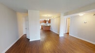 This single-story space in Tallahassee, Florida features a cohesive, open layout connected by rich wood-style flooring that runs throughout. The kitchen is well-appointed with warm medium-toned cabinetry offering generous storage, light-toned countertops, a peninsula that provides additional prep and seating space, and a full suite of white appliances including a refrigerator, range, dishwasher, and microwave. A textured ceiling and under-cabinet fluorescent lighting add functional detail to the kitchen area. Adjacent to the kitchen, the dining area is defined by a tasteful chandelier pendant, creating a distinct yet open zone within the shared space. The living area is spacious and bright, anchored by a large sliding glass door fitted with vertical blinds that invite natural light and provide views of the surrounding greenery. The open floor plan from the 3D model reveals a thoughtful arrangement of living spaces with clear sightlines throughout. The bathrooms are consistent in finish, each featuring warm wood-style flooring, a tub-shower combination with full tile surround in neutral tones, warm cabinetry with matching countertops, and chrome hardware accents. The overall aesthetic is clean, neutral, and functional, offering a practical and comfortable living environment.