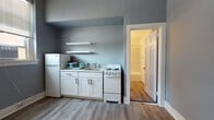 Located in the heart of Uptown Charlotte at 508 N Tryon St, this single-floor unit offers a thoughtfully arranged layout with clean, updated finishes throughout. The living area is finished with light-toned vinyl plank flooring and cool-gray painted walls, creating a calm, neutral palette. Natural light enters through multiple windows fitted with blinds, while classic cast-iron radiators add a charming, historic character that speaks to the building's architectural heritage. A window-mounted air conditioning unit provides additional climate control.

The kitchenette is efficiently designed, featuring white cabinetry with modern matte-black hardware, open floating shelves, a single-basin sink, and a compact electric range, offering all the essential cooking amenities in a streamlined footprint. A full-size refrigerator completes the kitchen space.

The bathroom is bright and well-appointed, showcasing marble-look tile surrounding the tub and shower combination, a white vanity with a round mirror, and warm lighting. Wood-look flooring ties the bathroom aesthetic to the rest of the unit seamlessly.

Overall, the space blends vintage building character—evident in the radiators and classic window proportions—with clean, contemporary updates, making it a practical and attractive option in one of Charlotte's most accessible urban neighborhoods.