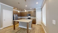 This two-story Denver, CO home delivers a thoughtfully organized layout spread across two floors. The more compact main level hosts the primary living and entertaining areas, including a contemporary kitchen featuring warm wood-toned flat-front cabinetry, stainless steel appliances, a built-in microwave, and a central island with a light quartz countertop illuminated by pendant lighting. Wood-look tile flooring and crown molding add a polished finish throughout the main level. The living room continues the cohesive aesthetic with neutral tones, a ceiling fan, and natural light from slatted windows.

The upper floor provides the majority of the living space, accommodating all three bedrooms. The carpeted secondary bedrooms are modestly sized, each featuring a window with natural light and closet access. The spacious primary bedroom includes its own well-appointed en suite bathroom with a dual-sink vanity featuring wood cabinetry, a large wall mirror, glass-enclosed shower with tile accents, and stone-look tile flooring. Additional bathrooms serve the remaining bedrooms and common areas. A dedicated laundry room with full-size washer and dryer units adds everyday convenience. Throughout, the home maintains a clean, modern aesthetic with neutral tones and consistent finishes.