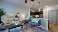 Located at 950 FM-2001 in Buda, Texas, this single-floor unit offers a thoughtfully designed open-concept layout that seamlessly connects the living, dining, and kitchen areas. The living room is filled with natural light streaming through large windows dressed with blinds and sheer curtains, creating a bright and welcoming atmosphere. Wood-style flooring runs throughout, complementing the neutral color palette and ceiling fans that add both comfort and style.

The kitchen is a standout feature, outfitted with rich dark espresso cabinetry, granite-look countertops, and a full suite of stainless steel appliances including a refrigerator, range, and microwave. A peninsula counter with pendant lighting above serves as both a workspace and casual seating area, bridging the kitchen and living spaces with functional elegance.

The bedroom is a serene retreat, featuring soft, neutral tones, a ceiling fan, and windows that invite natural light. Ample space accommodates a full furniture arrangement with ease.

The bathroom is clean and functional, featuring a tiled shower-tub combination, wood-style flooring, and crisp white finishes that lend a fresh, polished look. Overall, the unit presents a cohesive modern aesthetic with practical, well-considered design elements throughout.