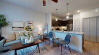 Located at 950 FM-2001 in Buda, Texas, this single-floor unit offers a thoughtfully designed open-concept layout that seamlessly connects the living, dining, and kitchen areas. The living room is filled with natural light streaming through large windows dressed with blinds and sheer curtains, creating a bright and welcoming atmosphere. Wood-style flooring runs throughout, complementing the neutral color palette and ceiling fans that add both comfort and style.

The kitchen is a standout feature, outfitted with rich dark espresso cabinetry, granite-look countertops, and a full suite of stainless steel appliances including a refrigerator, range, and microwave. A peninsula counter with pendant lighting above serves as both a workspace and casual seating area, bridging the kitchen and living spaces with functional elegance.

The bedroom is a serene retreat, featuring soft, neutral tones, a ceiling fan, and windows that invite natural light. Ample space accommodates a full furniture arrangement with ease.

The bathroom is clean and functional, featuring a tiled shower-tub combination, wood-style flooring, and crisp white finishes that lend a fresh, polished look. Overall, the unit presents a cohesive modern aesthetic with practical, well-considered design elements throughout.