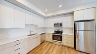 This well-designed 2-bedroom, 1-bathroom unit offers a thoughtful single-floor layout that maximizes functionality and comfort. The open living area features warm hardwood-style flooring, neutral white walls, and multiple windows fitted with blinds that allow for an abundance of natural light throughout the day.

The contemporary kitchen is a standout feature, showcasing a two-tone cabinet design with clean white upper cabinets and light wood lower cabinets, complemented by white countertops and a classic tile backsplash. The kitchen is fully equipped with stainless steel appliances, including a refrigerator, range, microwave, and dishwasher, as well as recessed lighting overhead.

Both bedrooms are carpeted and well-proportioned, with the primary bedroom offering direct access to a private balcony through sliding glass doors. The balcony features glass-panel railings and overlooks a tree-lined outdoor setting. The second bedroom includes a window with exterior views.

The bathroom is clean and efficiently laid out, featuring a full bathtub and shower combination, a modern vanity, and warm hardwood-style flooring. A stacked in-unit washer and dryer is conveniently located adjacent to the bathroom. A dedicated entrance and hallway connect all areas of the unit cohesively.