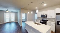 This 1-bedroom, 1-bathroom unit with a den in College Station, Texas offers a well-appointed, single-story layout designed for both comfort and functionality. The open-concept living and kitchen area serves as the heart of the home, anchored by a large center island with a quartz countertop, undermount sink, and stylish pendant lighting. The kitchen is outfitted with crisp white shaker cabinetry, stainless steel appliances including a French door refrigerator, electric range, and over-the-range microwave, all set against a neutral tile backsplash. Rich, dark hardwood-style flooring flows throughout the main living areas, adding warmth and visual continuity.

The living space opens to a dedicated den, which features its own ceiling fan and a set of French doors that invite natural light and provide access to the outdoors. The bedroom is carpeted for added comfort and includes a ceiling fan, while a bonus den or flex room with hardwood-style flooring and a bright window offers additional versatile space.

The bathroom features a quartz-topped vanity, wood-look flooring, a full soaking tub with oversized tile surround, and direct access to a walk-in closet. Neutral tones and clean finishes throughout create a modern, move-in-ready atmosphere.