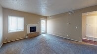 This single-floor residence offers a practical and comfortable layout designed for everyday living. The living room serves as the focal point of the home, featuring a wood-mantled fireplace set on a tile hearth, plush wall-to-wall carpeting, and a textured ceiling. A glass door in the living area allows natural light to flow in and provides access to the outdoors. The space is generously sized, offering ample room for a variety of furniture arrangements.

The kitchen is well-equipped with warm wood cabinetry, dark granite-style countertops, a double-basin sink, and tile flooring. A full suite of black appliances, including a refrigerator and range, is included. Open shelving near the upper cabinets adds additional storage and display space.

The bedrooms are carpeted and finished with neutral-toned walls, providing a calm and restful atmosphere. Each room benefits from windows that bring in natural light and views of the surrounding exterior. One bedroom includes a ceiling fan and access to a closet with built-in shelving.

The bathroom is clean and straightforward, featuring a full tub-and-shower combination with white tile surround. Throughout the home, consistent neutral wall tones and textured ceilings create a cohesive, understated aesthetic suited to a range of interior styles.