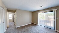 This efficiently designed 2-bedroom, 1-bathroom single-floor unit offers a practical and comfortable layout across a well-utilized footprint. The interior is finished throughout with warm neutral beige tones on the walls and white trim, creating a clean and consistent aesthetic.

The living room is carpeted and features a sliding glass door fitted with vertical blinds, allowing natural light to filter in while providing access to an outdoor balcony area with views of surrounding greenery. A textured ceiling and built-in HVAC vents are present throughout the unit.

The kitchen is equipped with warm-toned wooden cabinetry, dark granite-style countertops, a double stainless steel sink, and a full appliance suite including an electric range and over-the-range microwave. Wood-look flooring runs through the kitchen and extends into adjacent areas, adding a durable and attractive touch.

The primary bedroom is a comfortable size, featuring carpet, a ceiling fan with light fixture, a window for natural light, and direct access to a dedicated closet with shelving. The second bedroom is also carpeted with neutral walls and a separate door.

The bathroom is well-appointed with a single-sink vanity featuring dark countertops and wooden cabinetry, a full-size soaking tub with shower combination, and wood-look flooring. A separate dining area and closet round out the unit's practical layout.