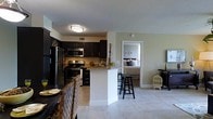 This single-floor residence offers a well-designed open-concept layout that connects the kitchen, dining, and living areas into one cohesive, functional space. The kitchen is a standout feature, outfitted with dark espresso cabinetry that contrasts beautifully against light-toned walls and neutral tile flooring. Stainless steel appliances — including a refrigerator, range, and microwave — bring a modern, polished feel to the space. A granite-topped peninsula with bar stool seating serves as both a prep area and a casual dining spot, making it ideal for entertaining or everyday use. The open flow of the layout ensures the kitchen remains visually connected to the surrounding living areas, creating an airy and welcoming atmosphere. Light tile flooring extends throughout the main living spaces, contributing to a clean and cohesive aesthetic. A doorway from the main living area provides direct access to the bedroom, which features warm, neutral tones and comfortable furnishings. The overall ambiance of the space is modern yet approachable, with thoughtful design choices — from the dark cabinetry to the light countertops and flooring — that balance contrast and cohesion throughout.