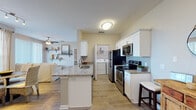 Located at 200 Village Blvd in Davenport, Florida, this single-floor residence offers a well-designed open-concept layout that seamlessly connects the kitchen, dining, and living areas. The kitchen is outfitted with white shaker-style cabinetry, granite countertops, stainless steel appliances including an electric range and microwave, a subway tile backsplash, and a central island with a sink — providing both functionality and style. Light wood-look flooring runs throughout the main living areas, creating a bright and cohesive feel. A dedicated laundry area with a washer and dryer is conveniently accessible directly from the kitchen. The dining nook features a large window that fills the space with natural light and offers pleasant outdoor views. The living room is anchored by sliding glass doors that open to a balcony, framing scenic views of the surrounding landscape, while a ceiling fan adds comfort overhead. The bedrooms are carpeted and restful, each featuring ceiling fans and natural light from well-positioned windows. The bathrooms feature granite-topped white vanities, wood-look flooring, and tub-shower combinations. Throughout the residence, a neutral color palette and consistent finishes create a calm, inviting atmosphere well-suited for comfortable everyday living.