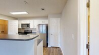 Located at 1115 Jasmine Cove Cir in Simpsonville, SC, this 2-bedroom, 2-bathroom residence offers a practical and comfortable layout across a single floor. The open-concept kitchen and living room serve as the heart of the home, featuring rich hardwood-style flooring, white cabinetry with modern hardware, dark granite-style countertops, and stainless steel appliances including a refrigerator, electric range, and built-in microwave. French doors in the living area flood the space with natural light and provide access to a private balcony, while a ceiling fan adds comfort overhead. A tray ceiling detail adds an architectural touch to the living space. Both bedrooms are carpeted and include ceiling fans, with natural light streaming through sizable windows. The primary bedroom is generously sized and connects to ample closet space. In total, five closets throughout the home provide exceptional storage. The two bathrooms are finished with wood-style flooring, white vanities, and full tub/shower combinations. A dedicated utility room and staircase complete the layout. The neutral color palette and clean finishes throughout create a bright, move-in-ready atmosphere.