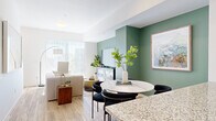 This well-designed three-story townhome in Longmont, Colorado offers a thoughtful layout spread across three levels, combining modern aesthetics with practical functionality. The entry level provides an attached garage and a flexible office space, ideal for working from home. The main living floor showcases a bright, open-concept design where the living room, dining area, and kitchen flow seamlessly together. The living room features sage green accent walls, warm hardwood-style flooring, and large sliding glass doors that fill the space with natural light. The contemporary kitchen is appointed with slate-blue cabinetry, granite countertops, a central island, stainless steel appliances, and a subway tile backsplash. A sleek half bathroom with a floating vanity and wood-look flooring completes this level. Upstairs, the two bedrooms are carpeted and bathed in natural light from large windows offering pleasant outdoor views. The primary bedroom connects directly to an en-suite bathroom featuring granite countertops and modern fixtures. A second full bathroom with granite countertops and a shower serves the additional bedroom. Throughout the home, clean white walls, recessed lighting, and ceiling fans contribute to a fresh, contemporary ambiance.