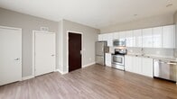 Located on the fourth floor at 2255 Wisconsin Ave NW in the heart of Washington, DC's Georgetown neighborhood, this modern apartment offers a thoughtfully designed single-level layout with clean lines and contemporary finishes throughout. The open-concept living and kitchen area creates a seamless flow, anchored by warm wood-tone luxury vinyl plank flooring that extends throughout the main living spaces. The kitchen is outfitted with sleek, high-gloss white cabinetry extending to the ceiling for ample storage, complemented by light-toned countertops and a full suite of stainless steel appliances, including a refrigerator, electric range, built-in microwave, and dishwasher. A single-basin sink with a modern faucet completes the functional workspace. The open living area is bathed in natural light from a large sliding glass door that leads to an outdoor balcony, offering views of the surrounding neighborhood. The bathroom features light large-format tile flooring, a combined tub and shower with full white tile surround, and a wood-accented vanity. Neutral warm-gray walls throughout the unit provide a versatile backdrop, while recessed lighting and a clean, minimalist aesthetic give the space a polished, move-in-ready feel.