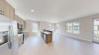 This contemporary single-floor residence showcases a clean, modern design with an emphasis on open living and natural light. The heart of the home is a spacious open-concept kitchen and living area, where light hardwood-style flooring flows seamlessly underfoot. The kitchen is anchored by a peninsula with a white quartz countertop, an undermount sink, and stainless steel appliances including a range with oven, built-in microwave, and dishwasher. Light wood cabinetry with a dark tile backsplash adds warmth and contrast, while multiple windows frame views of the surrounding neighborhood and flood the space with daylight. The open living area extends naturally from the kitchen, offering a bright and versatile layout. The bedrooms feature plush carpeting and large windows that invite natural light, with one bedroom offering a closet and serene exterior views. The bathrooms are finished in a consistent modern palette, featuring warm wood-toned vanities with white quartz countertops, undermount sinks, framed mirrors, and light-toned flooring. The overall ambiance is clean, bright, and contemporary, with a neutral color scheme that creates a welcoming and adaptable living environment throughout.