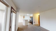 Located at 4034 Idlewild Loop in Coeur d'Alene, Idaho, this single-floor residence offers a practical and comfortable layout designed for everyday living. The open-concept living and dining area is finished with neutral-toned carpet and flows seamlessly into the kitchen, which is defined by a peninsula counter — ideal for casual dining or food prep. The kitchen itself is well-equipped with warm honey-toned wood cabinetry, light countertops, hardwood-style flooring, a black electric range, and a full-size refrigerator, providing ample storage and workspace. A built-in range hood and overhead fluorescent lighting keep the kitchen bright and functional. The living area features a door leading to an outdoor area, allowing natural light to filter in. The residence includes multiple bedrooms, each carpeted and featuring sliding windows that bring in natural light. Individual heating units are present in the bedrooms, ensuring comfort year-round. The bathrooms are clean and efficiently designed, featuring hardwood-style flooring, a tub-shower combination, a vanity with a single sink and mirror, and chrome fixtures. Throughout the space, a consistent neutral color palette and clean finishes contribute to a bright, move-in-ready atmosphere.