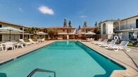 Located at 14300 Mulberry Dr in Whittier, California, this residential community combines classic architectural design with well-maintained outdoor amenities. The buildings feature a Spanish-influenced style with white stucco exteriors, arched entryways, wrought iron balcony railings, and warm terracotta-toned rooflines that give the property a cohesive and inviting character.

The centerpiece of the community is a generously sized outdoor swimming pool, framed by a spacious concrete deck furnished with lounge chairs and shaded umbrella tables — ideal for relaxing under the Southern California sun. The pool area is enclosed by a wrought iron fence, providing both security and an open, airy feel.

The property's interior courtyard is a standout feature, showcasing a circular green lawn with a mature tree at its center, creating a tranquil focal point surrounded by a curved walkway. Additional landscaped areas throughout the grounds include manicured grass, shrubs, and mature shade trees that contribute to the lush, park-like atmosphere.

Balconies accessible from the upper-level units overlook the courtyards, offering pleasant outdoor views. The gated grounds and thoughtfully arranged outdoor spaces reflect a community designed with comfort and connectivity in mind, all set beneath the bright, clear skies characteristic of the greater Los Angeles area.