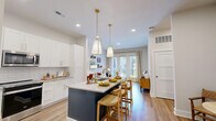 Located in Marietta, GA, this well-appointed 2-bedroom, 2-bathroom residence offers a thoughtfully designed single-level floor plan with modern finishes throughout. The open-concept kitchen and living area serves as the heart of the home, showcasing white shaker cabinetry with gold hardware, granite countertops, a striking navy center island with seating, white subway tile backsplash, and stainless steel appliances. Dual pendant lights with gold accents illuminate the island, adding a contemporary touch. The living area flows seamlessly toward French doors that open onto a private balcony, filling the space with natural light. Hardwood-style flooring runs throughout the main living areas, complementing the bright, neutral palette. The two bedrooms feature plush carpet and ample natural light, with the primary bedroom offering generous proportions and access to a well-appointed en-suite bathroom. The bathrooms are finished with marble-look tile, including a glass-enclosed walk-in shower in one and a soaking tub with floor-to-ceiling marble surround in the other. Additional conveniences include three closets, a dedicated laundry area, a utility room, and a connecting hallway that ensures a logical, functional layout throughout the home.