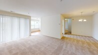 Located at 5726 Sugar Maple Ct, Apt B12 in Frederick, Maryland, this single-floor residence offers a clean, well-organized layout designed for comfortable everyday living. The open living and dining area is generously sized, featuring plush wall-to-wall carpeting, large windows with vertical blinds that allow abundant natural light, and an elegant pendant chandelier that adds a refined touch to the space. The galley-style kitchen is efficiently designed with white cabinetry, a coil-burner electric range, dishwasher, and refrigerator, all set above warm hardwood-style flooring. Louvered closet doors adjacent to the kitchen provide additional storage convenience. The unit includes multiple bedrooms, each carpeted and bathed in natural light through large windows offering views of surrounding greenery. One bedroom features a walk-in closet with built-in shelving and direct access to a private en-suite bathroom. Both bathrooms are finished in a crisp, clean white palette with tiled tub-shower combinations, white vanities, and light tile flooring. Throughout the unit, neutral tones and a bright, airy atmosphere create a versatile canvas well-suited to a variety of interior styles.